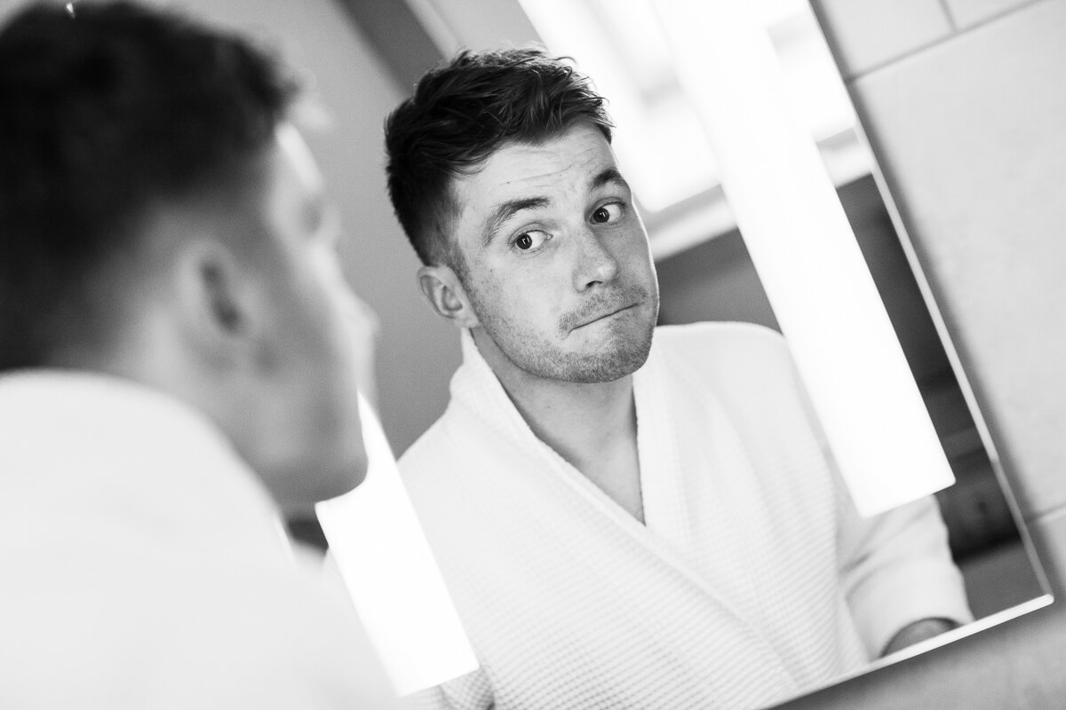 groom pulling a funny in face in the mirror wearing white dressing gown