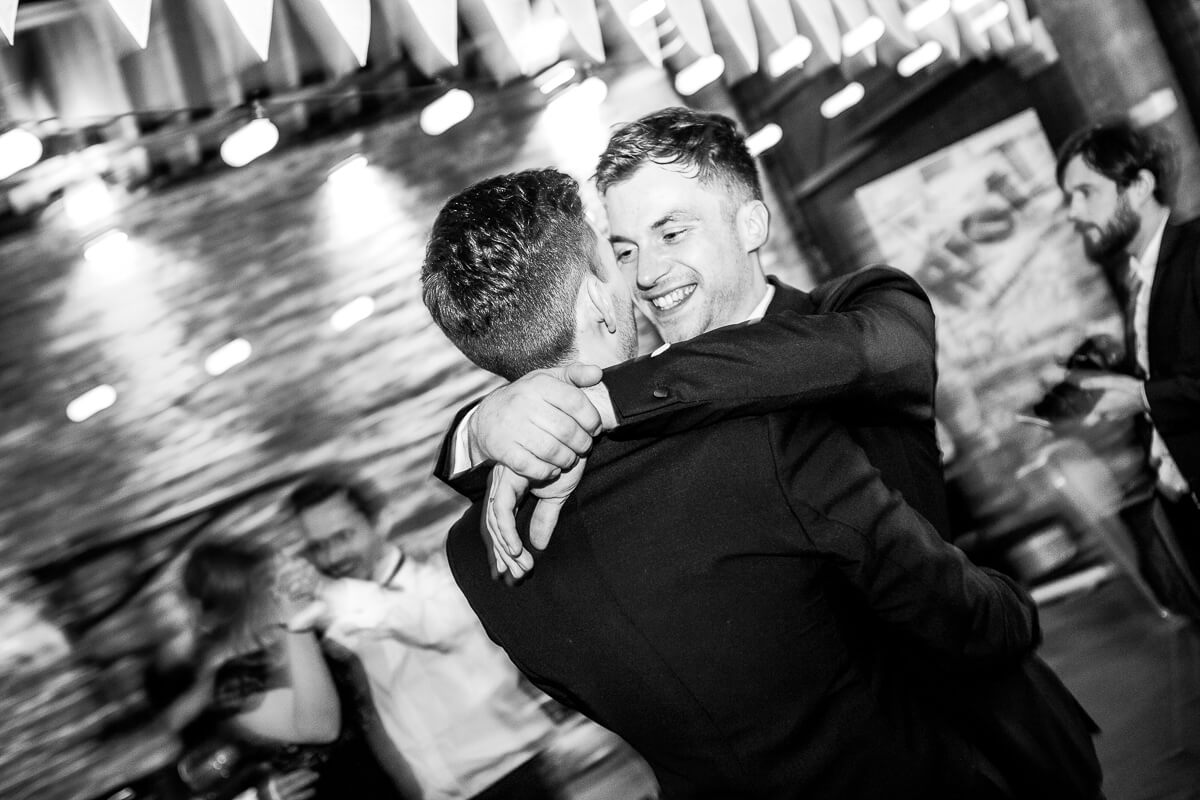 groom with arms round the neck of his new husband as their do first dance