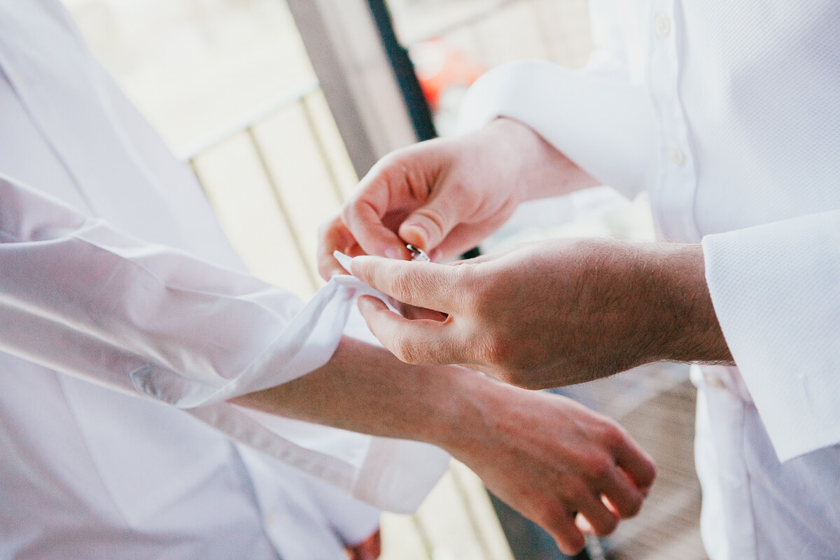 close up of two grooms doing up cufflinks for each other