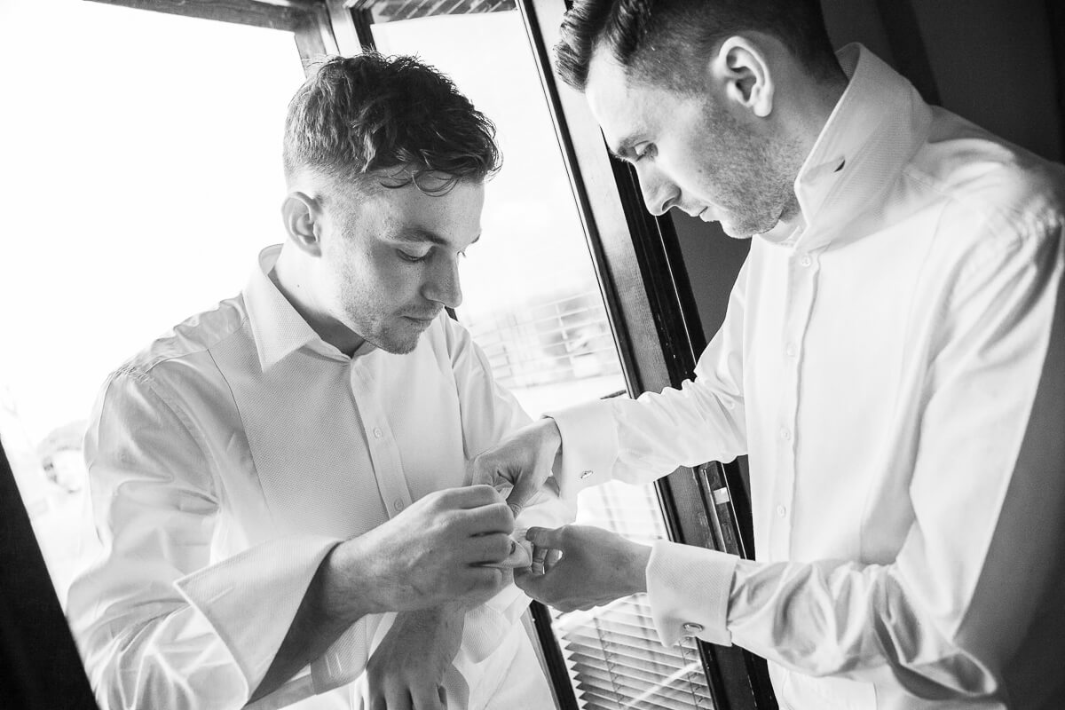 two grooms doing up cufflinks