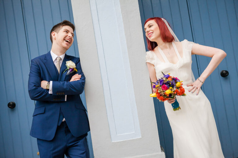bride and groom smile at each other either side of pillar with blue doors behind them
