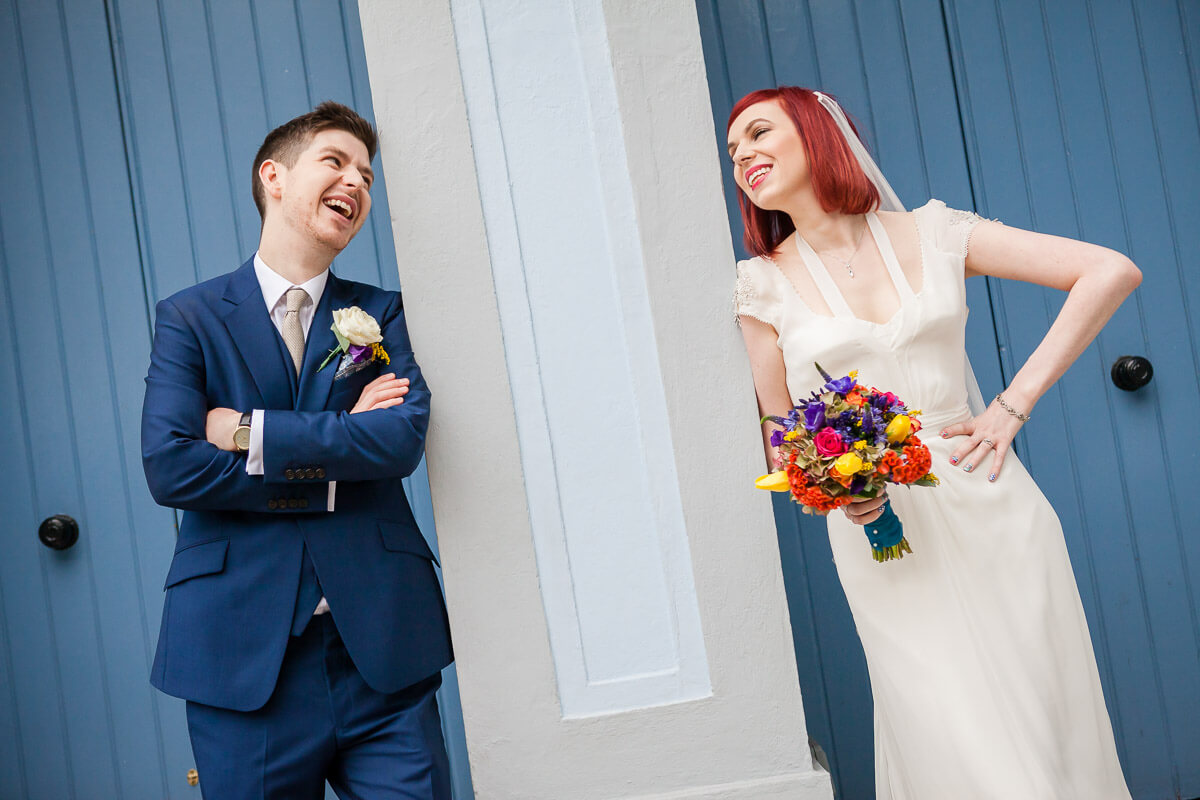 bride and groom smile at each other either side of pillar with blue doors behind them