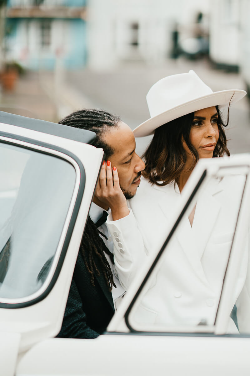 bride and groom sitting in passenger seat of classic car bride sitting on groom's lap holding the side of his face