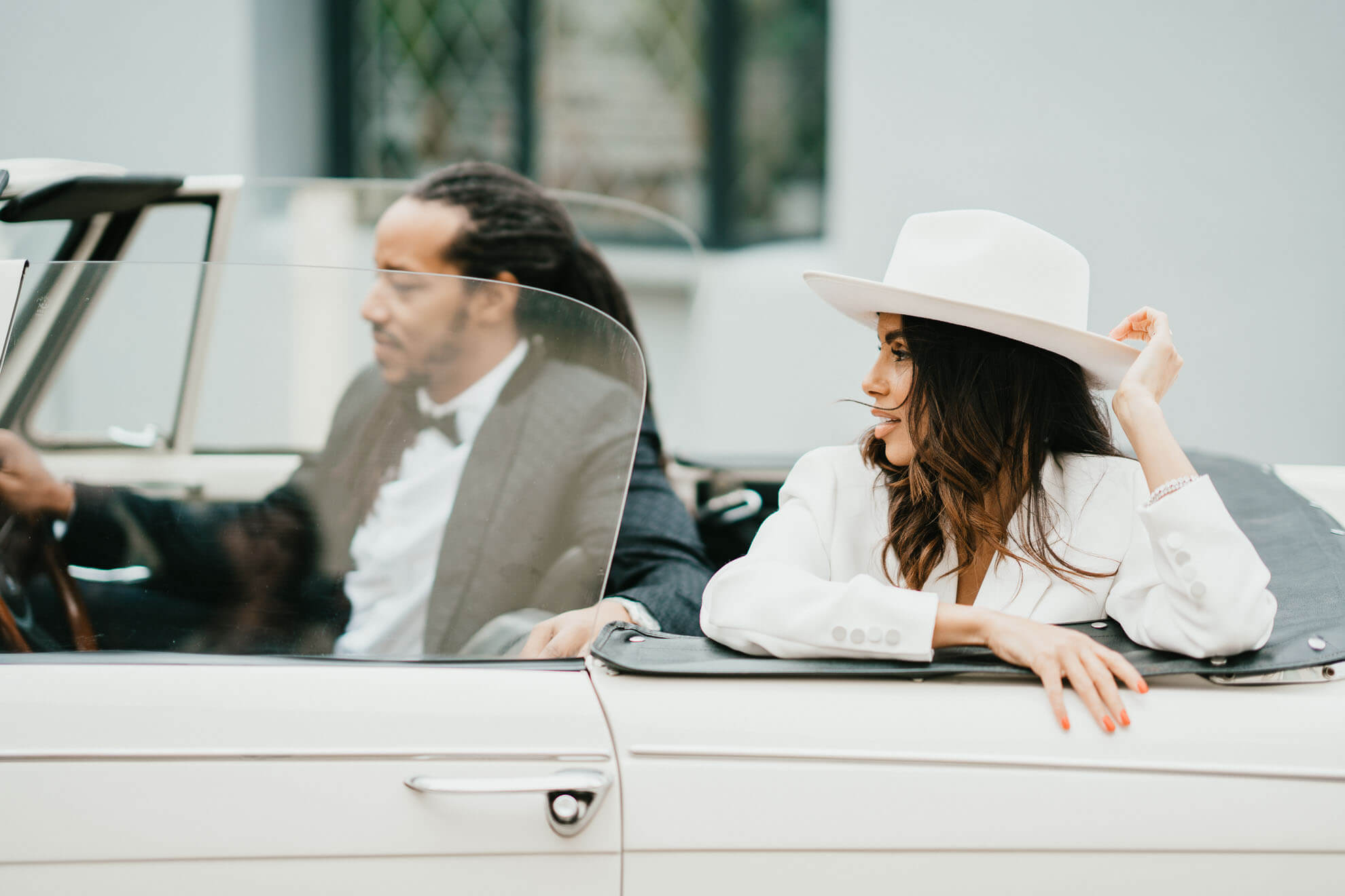 groom and bride in classic vintage car with groom at drivers wheel and bride in back looking dam cool