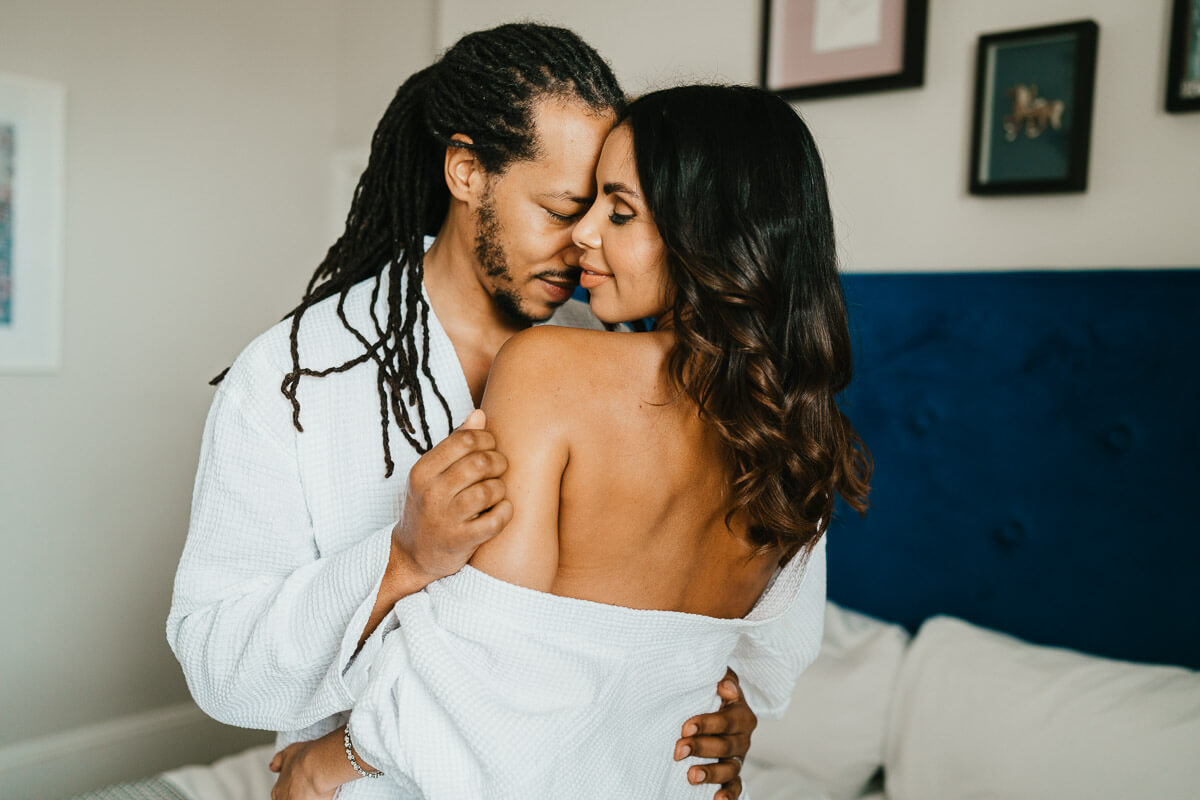 bride and groom getting ready in hotel room with grooms face resting against her face arms on shoulders