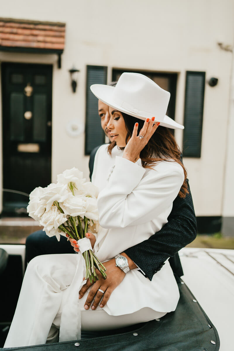 groom puts arms around waist of bride as she looks down touching the sit of her hat