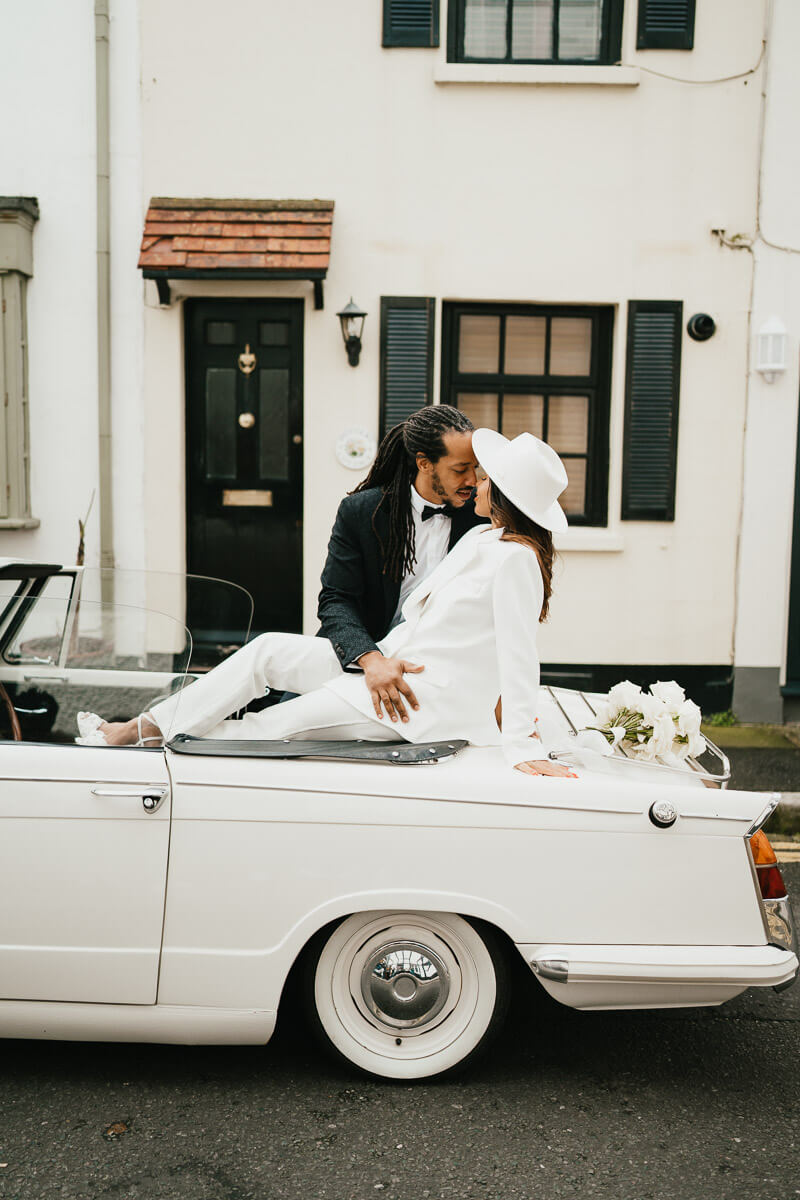 bride sits back with feet up on back of classic car while groom leans in for a kiss