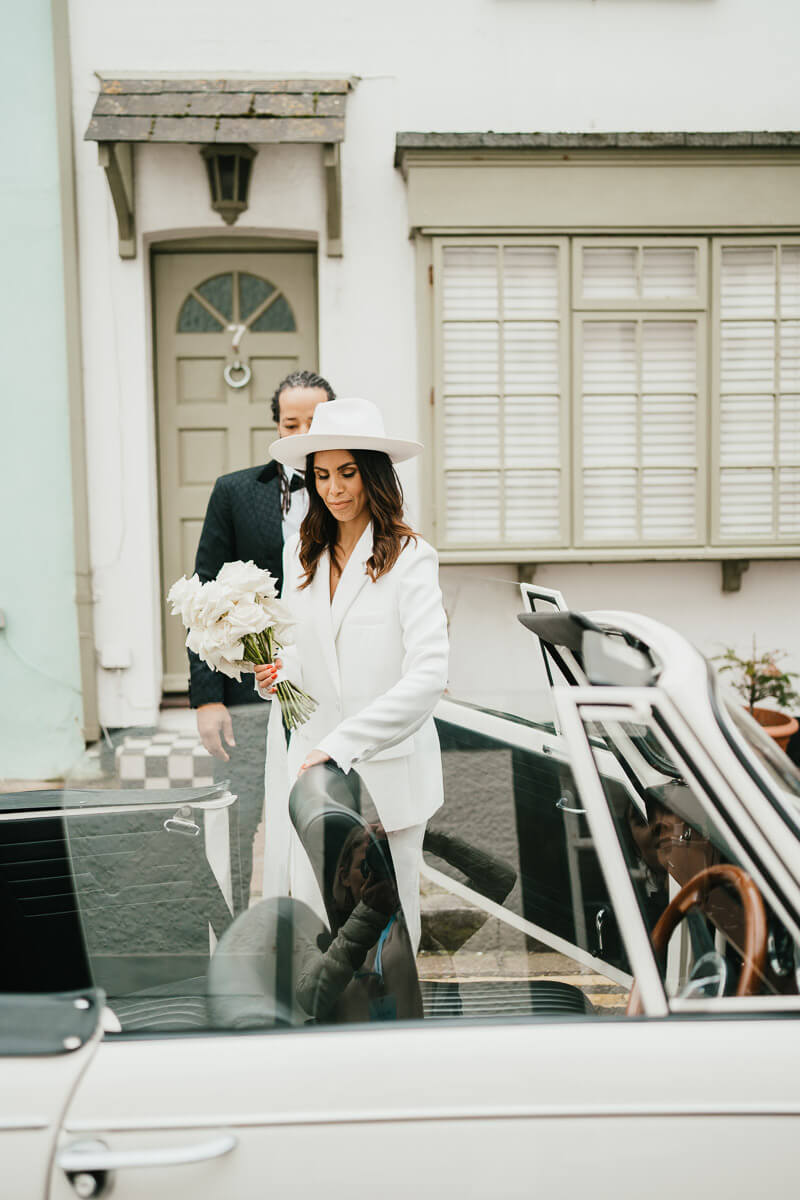 groom opening car door for bride to get into the back of the classic convertible car