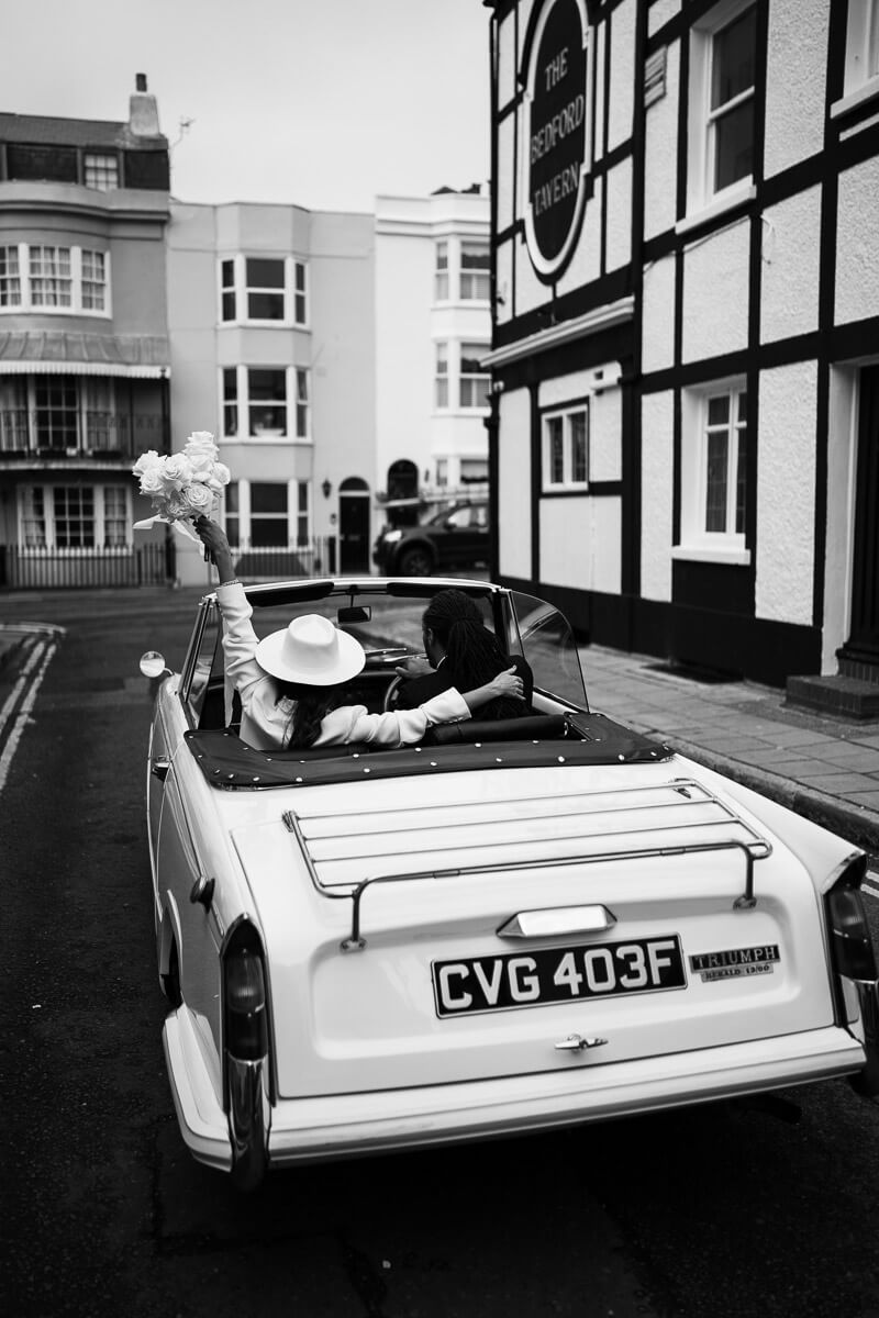 shot of the back of the convertible classic car with brides arm around groom as he drives off and she's holding up her flowers.