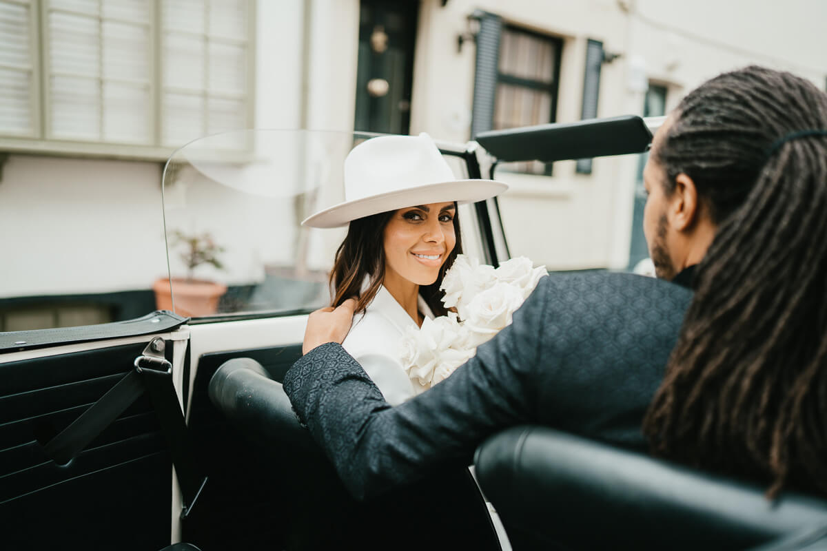 shot from the back seat of the car with groom putting arm on bride's shoulder as she looks back and smiles at the camera