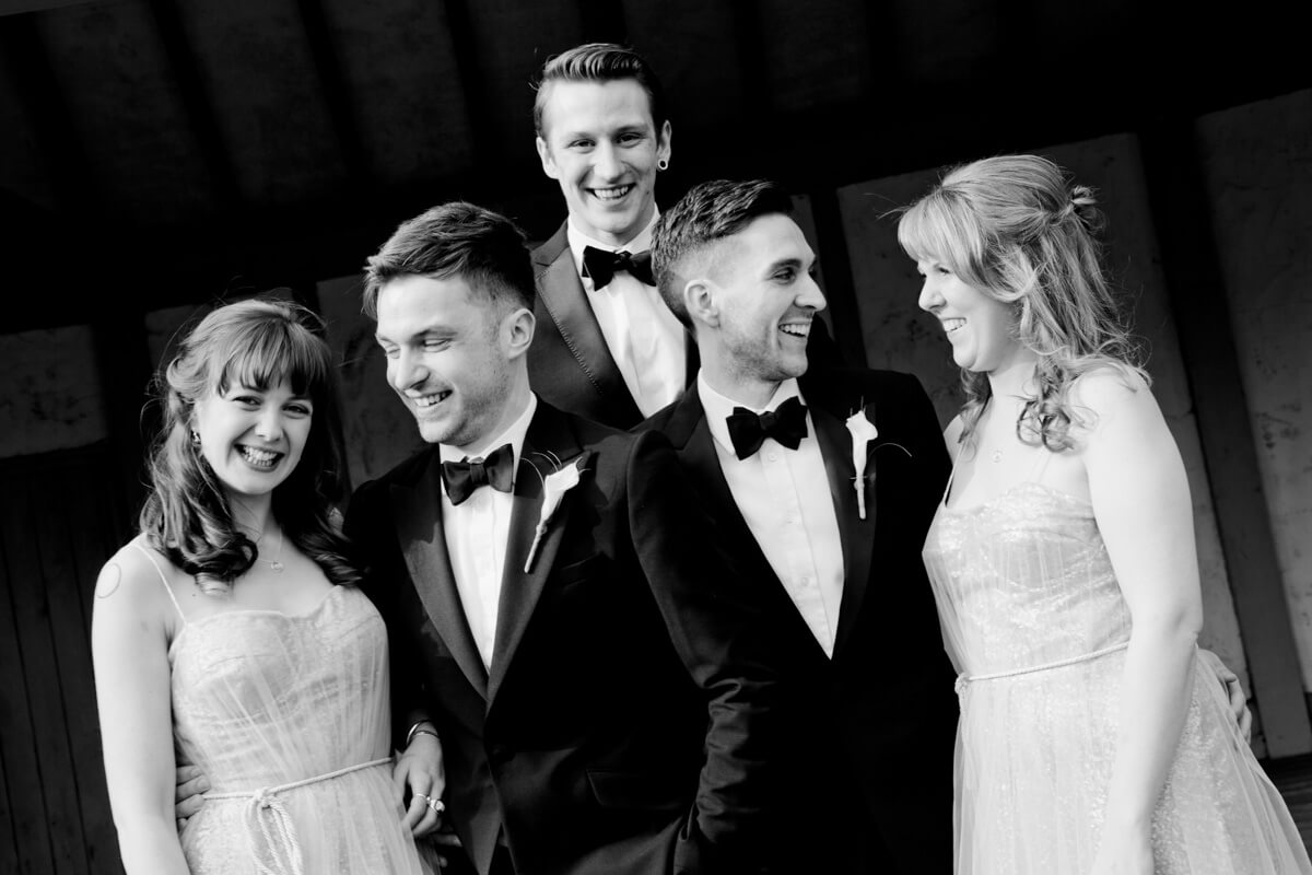 two grooms and two bridesmaids looking at each other smiling