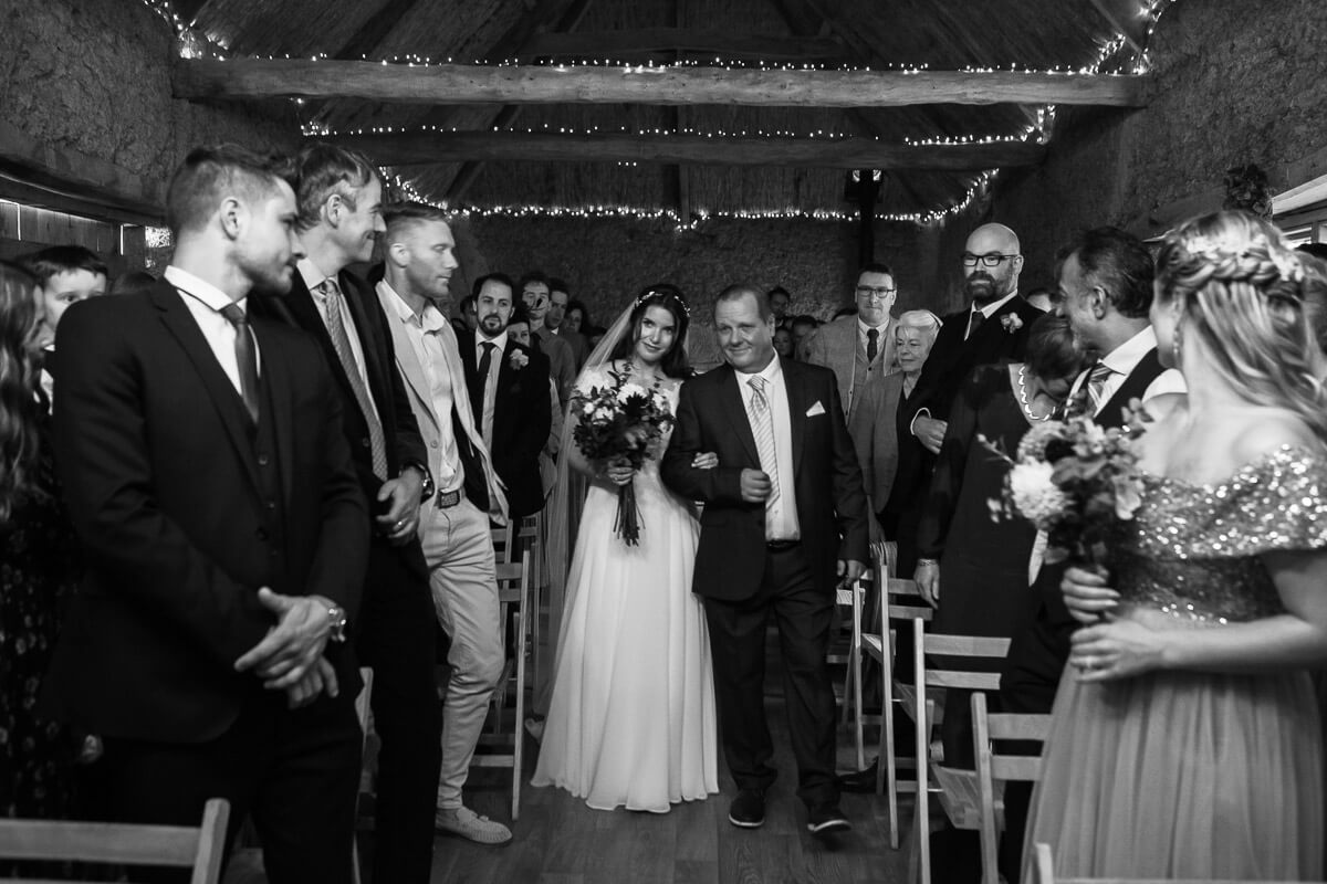 bride walking down the aisle with her father with guests either side