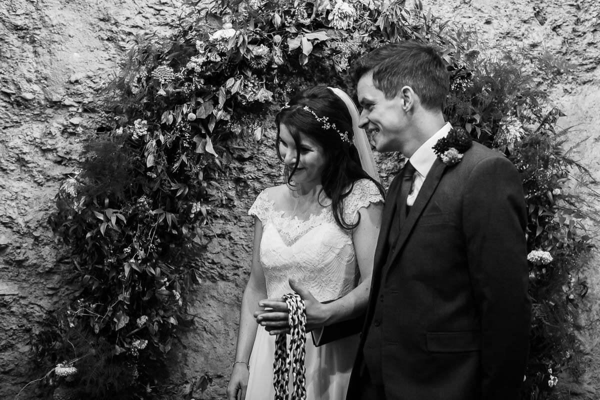 bride and groom standing side by side with handfasting ropes around their hands
