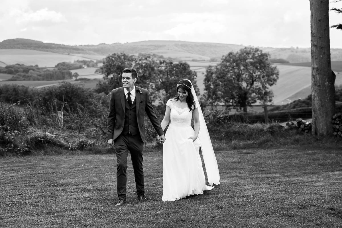 black and white shot of bride and groom walking hand in hand across lawn