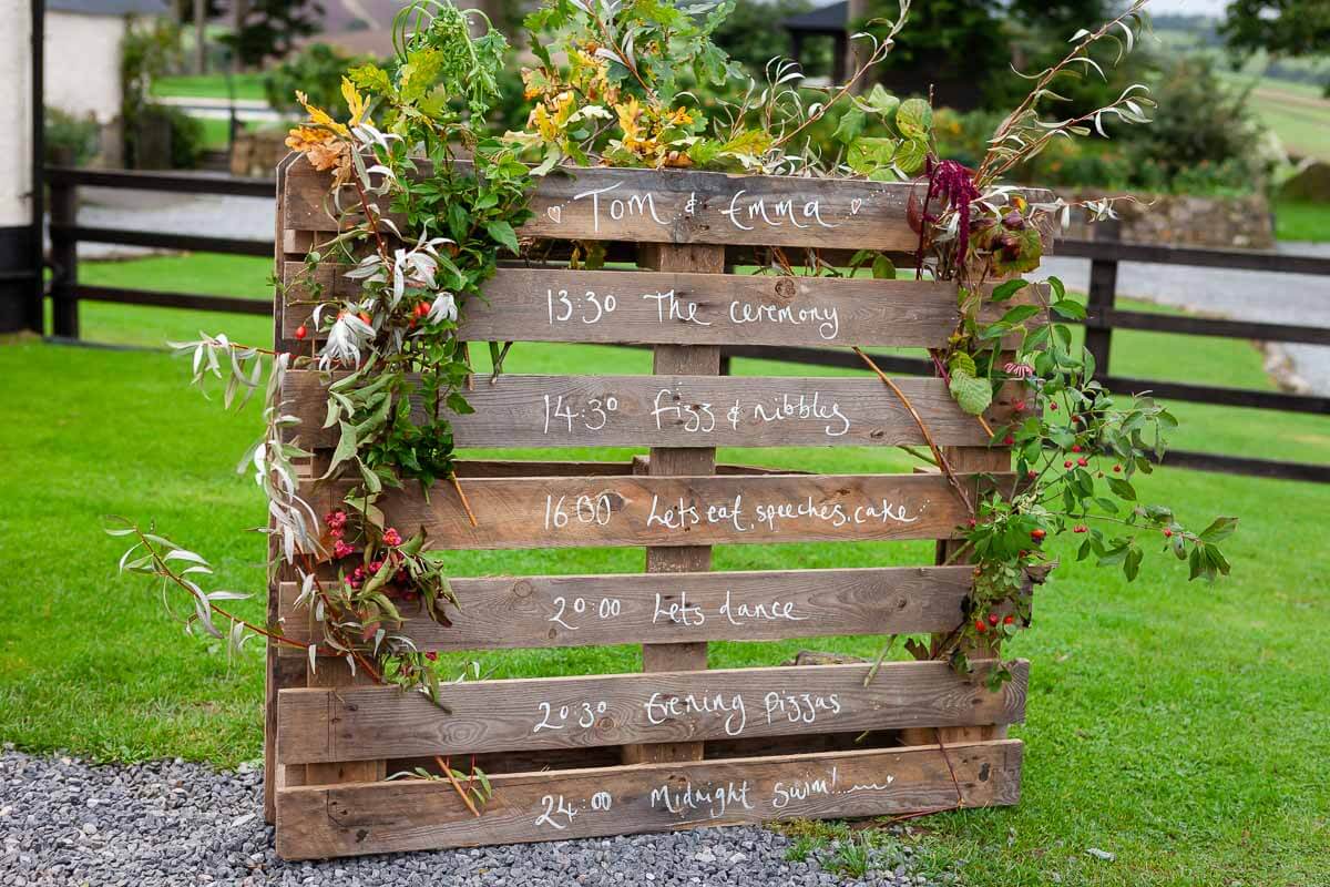 rustic timeline of day board made out of wood draped in greenery and flowers
