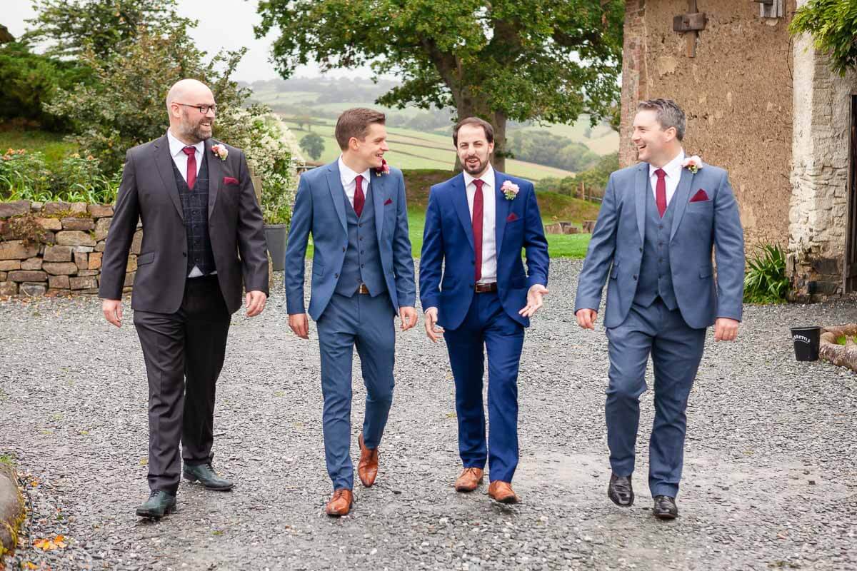 Groom and his groomsmen walking along stone pathway all looking at each other smiling