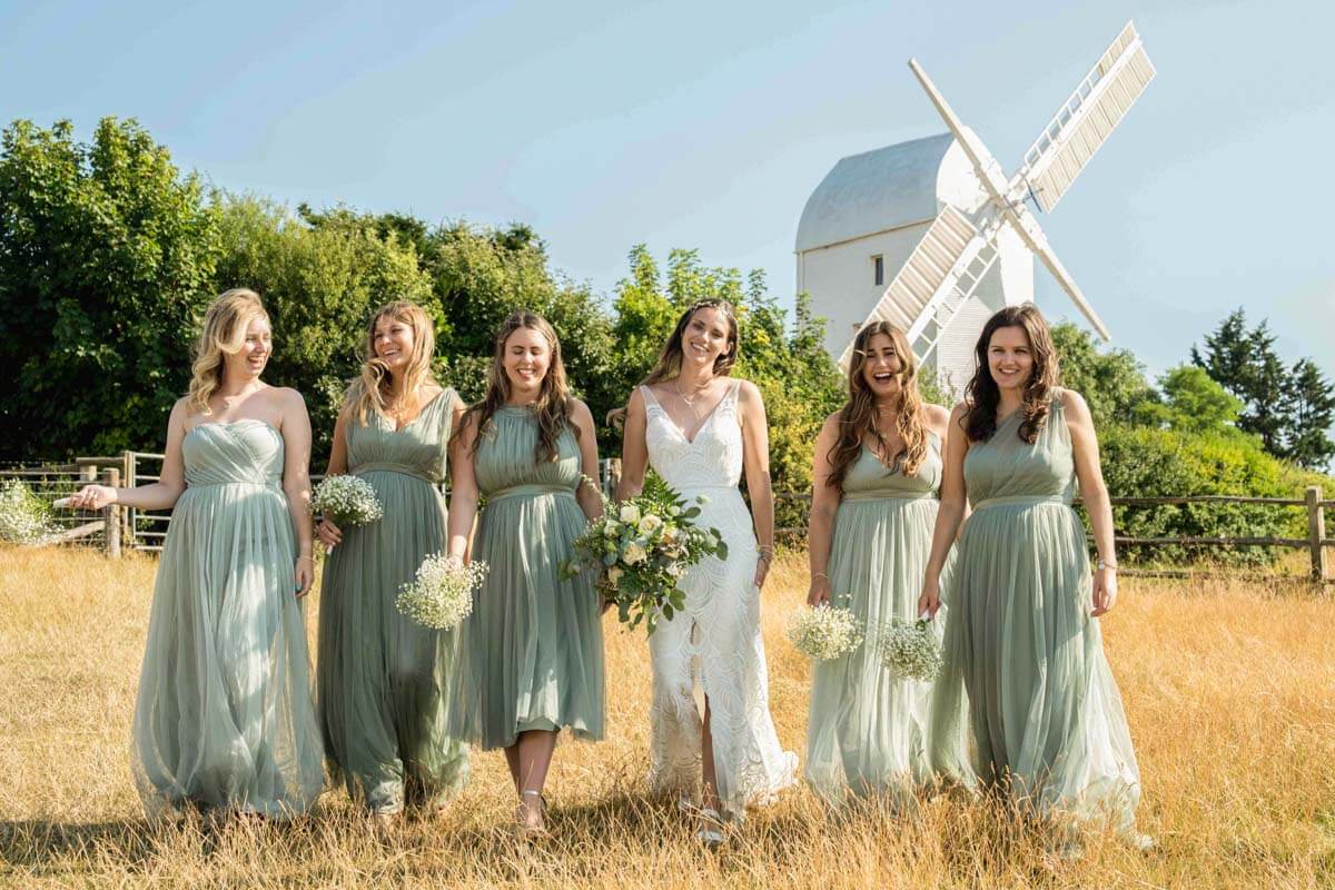 bride and bridesmaids walking towards the camera with windmill in background