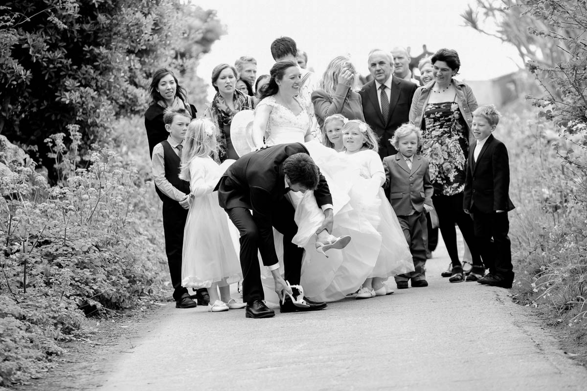 wedding party walking along country lane with groom stopping to bend down and put bride's shoe back on