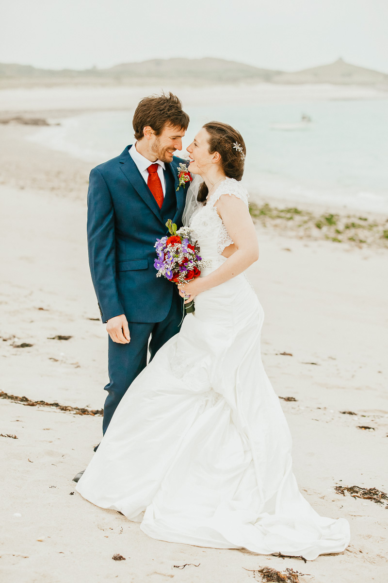 bride and groom on beach looking to each other chatting and smiling