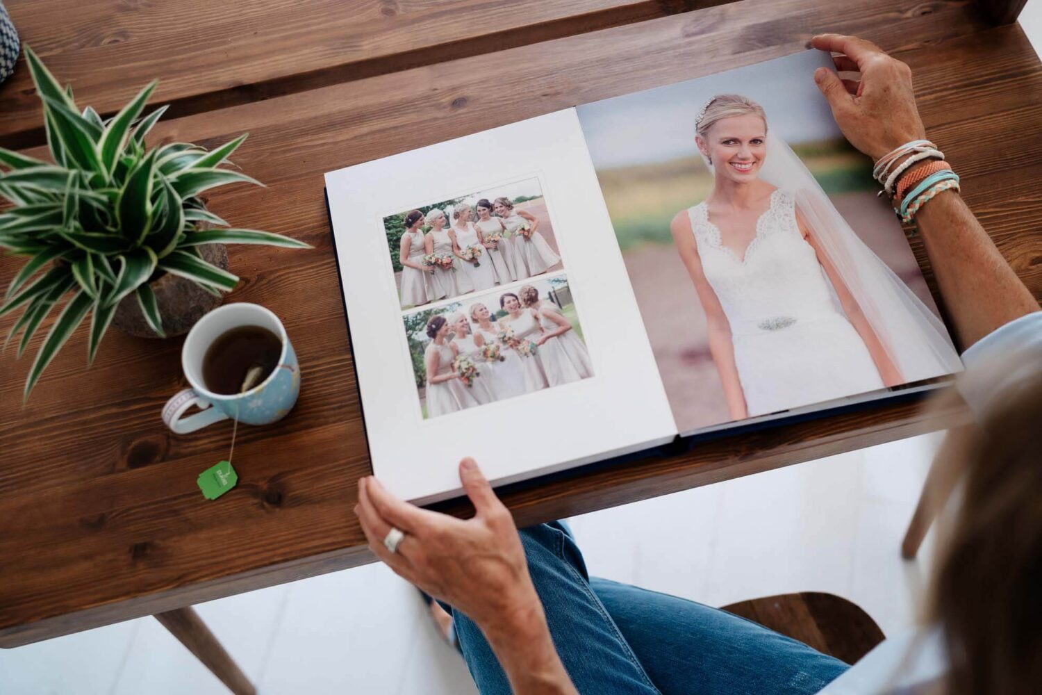 over head shot of professional wedding album and hand about to turn a page. cup of tea and plant in the corner of a lovely wooden desk