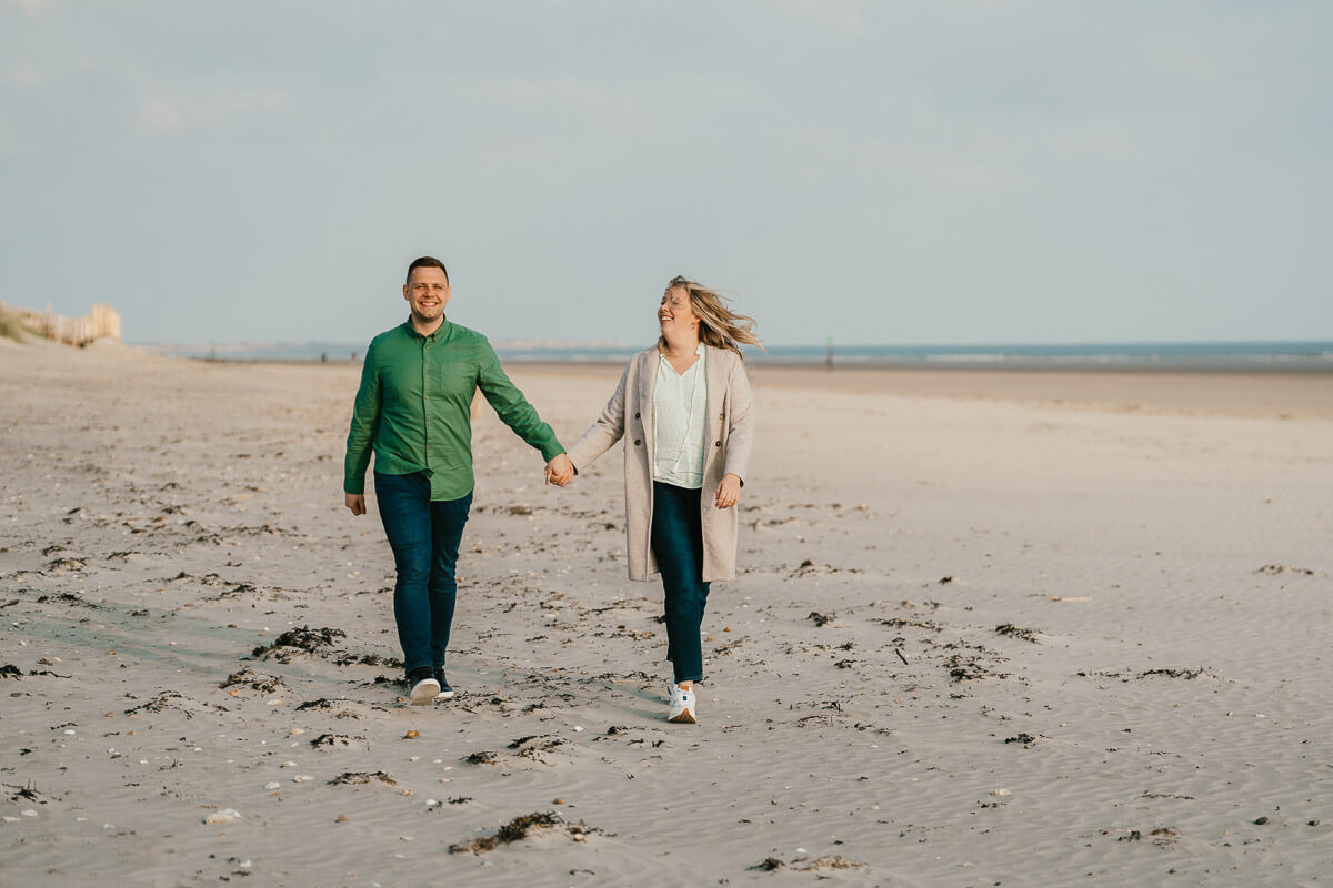 man and woman walking along beach hand in hand smiling and looking up