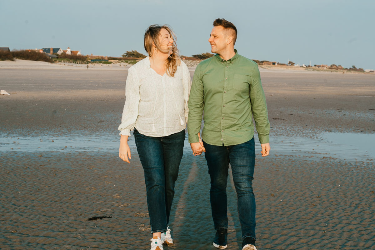couple walking through beach on low tide looking at each other holding hands