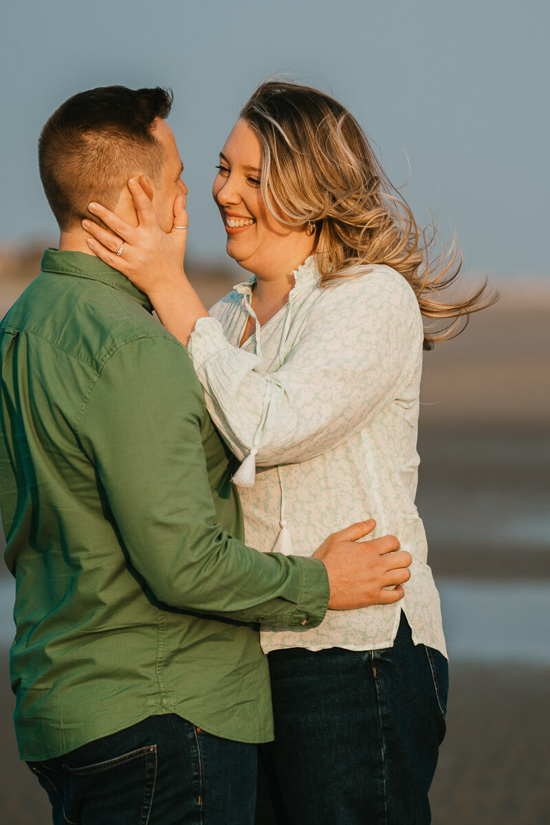 woman cups hand around man's face drawing him in closer standing on beach