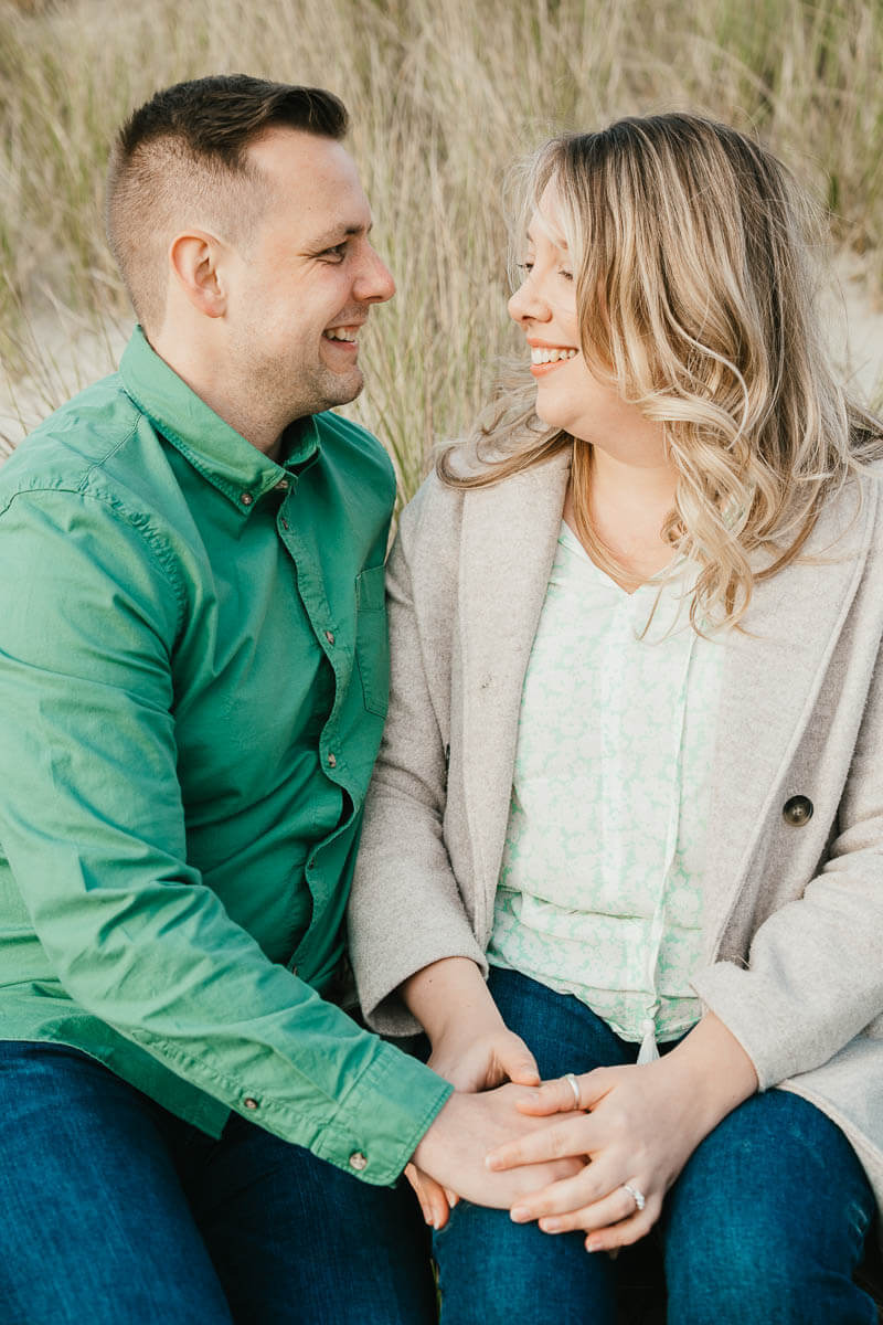 couple sitting on sand holding hands and looking at each other