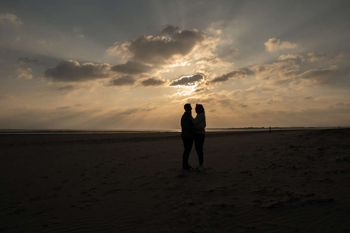 silhouetted couple standing against setting sun on beach