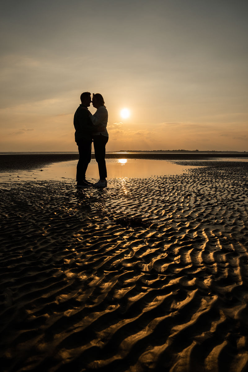 couple standing in the shallow waters with the sun lighting up the sand