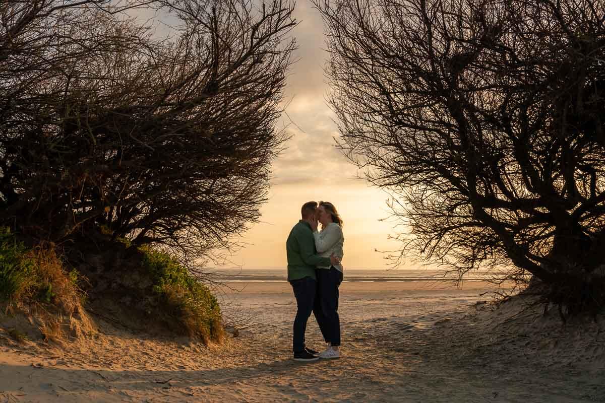 couple standing at the entrance to the beach with trees either side of them