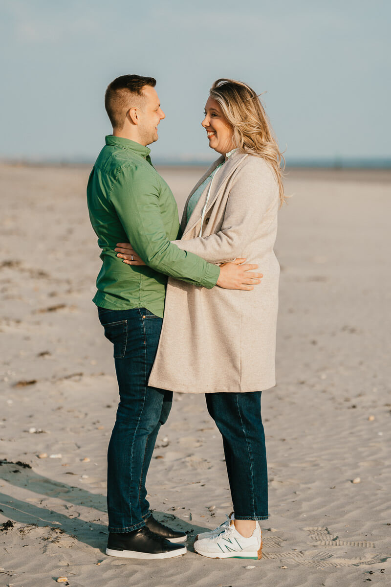 couple with arms around waist looking at each other standing on beach