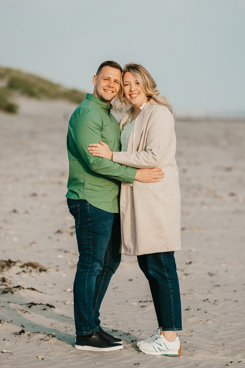 man and woman standing looking at camera with sides of heads touching and arms around each other