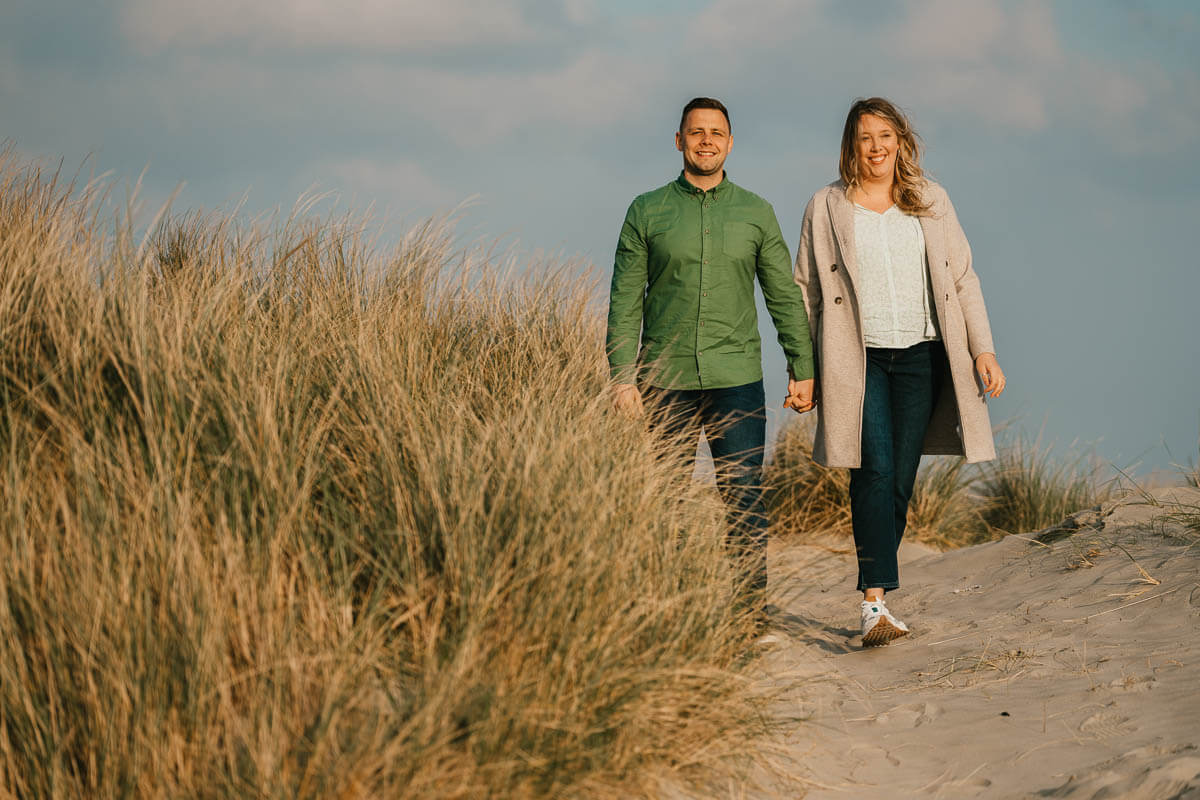 couple walking throughlong grass and sand dunes holding hands