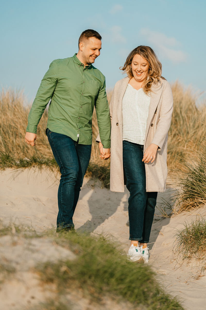 couple walking through grass and sand dunes holding hands