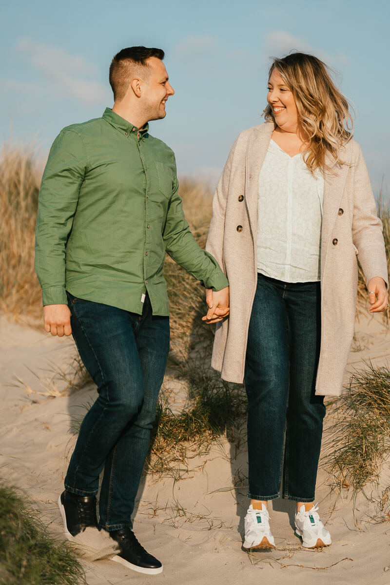 couple looking at each other holding hands walking through sand dunes