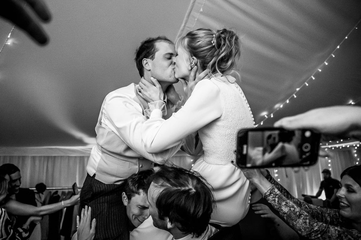 bride and groom on guests shoulders on dance floor kissing 
