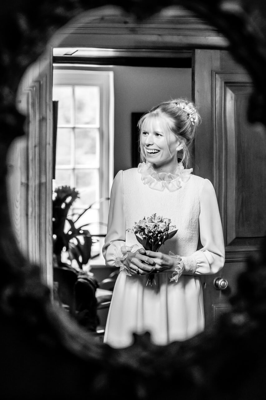 bride holding small bouquet of flowers smiling looking to the left taken in mirror reflection