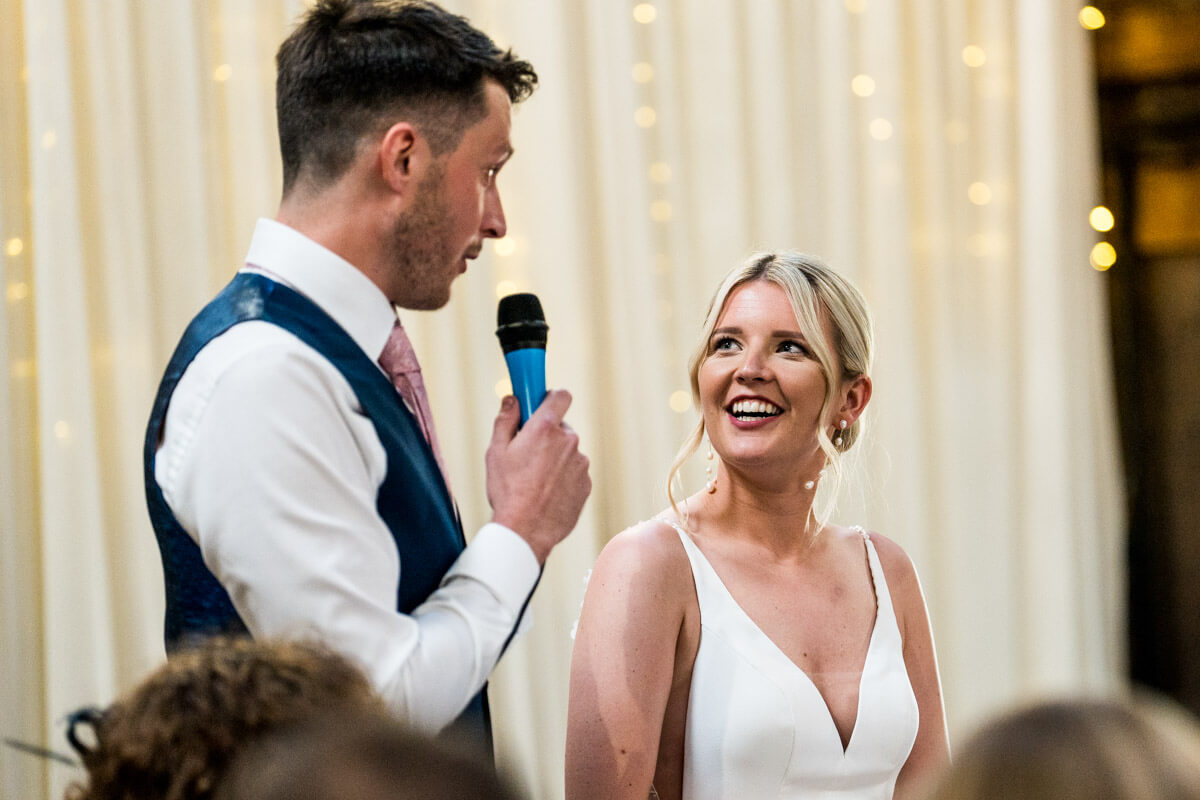 groom delivering speech while bride looks on smiling