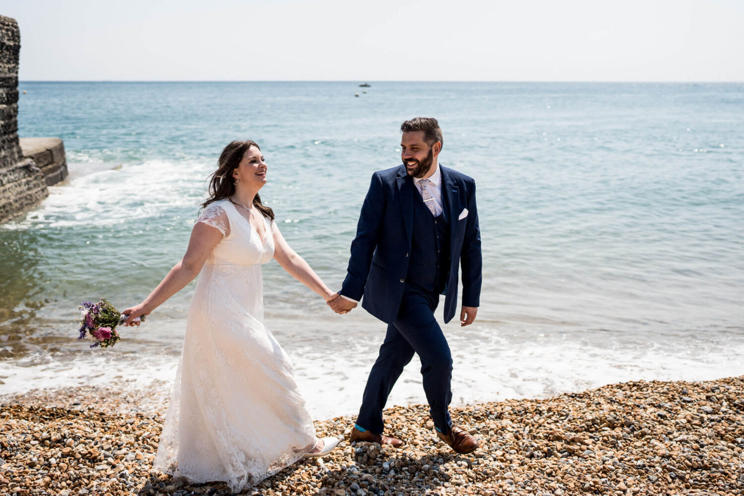 groom leading bride across Brighton pebble beach