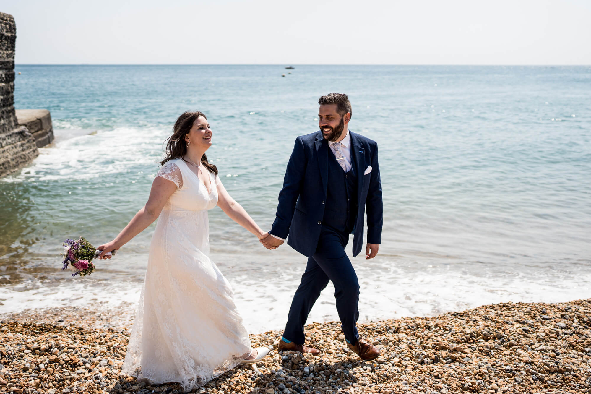 groom leading bride across Brighton pebble beach