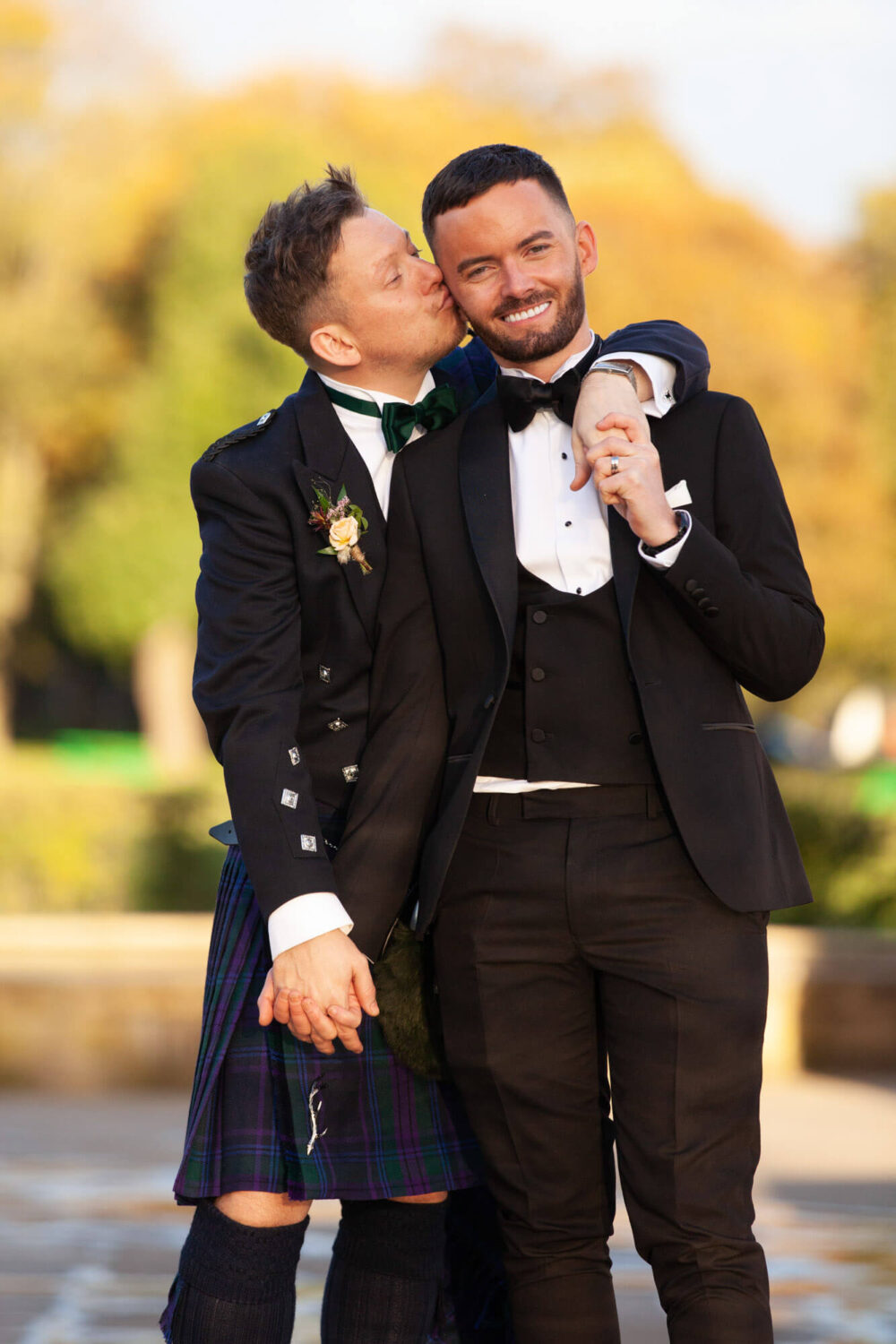two guys linking hands one kissing the other ones cheek