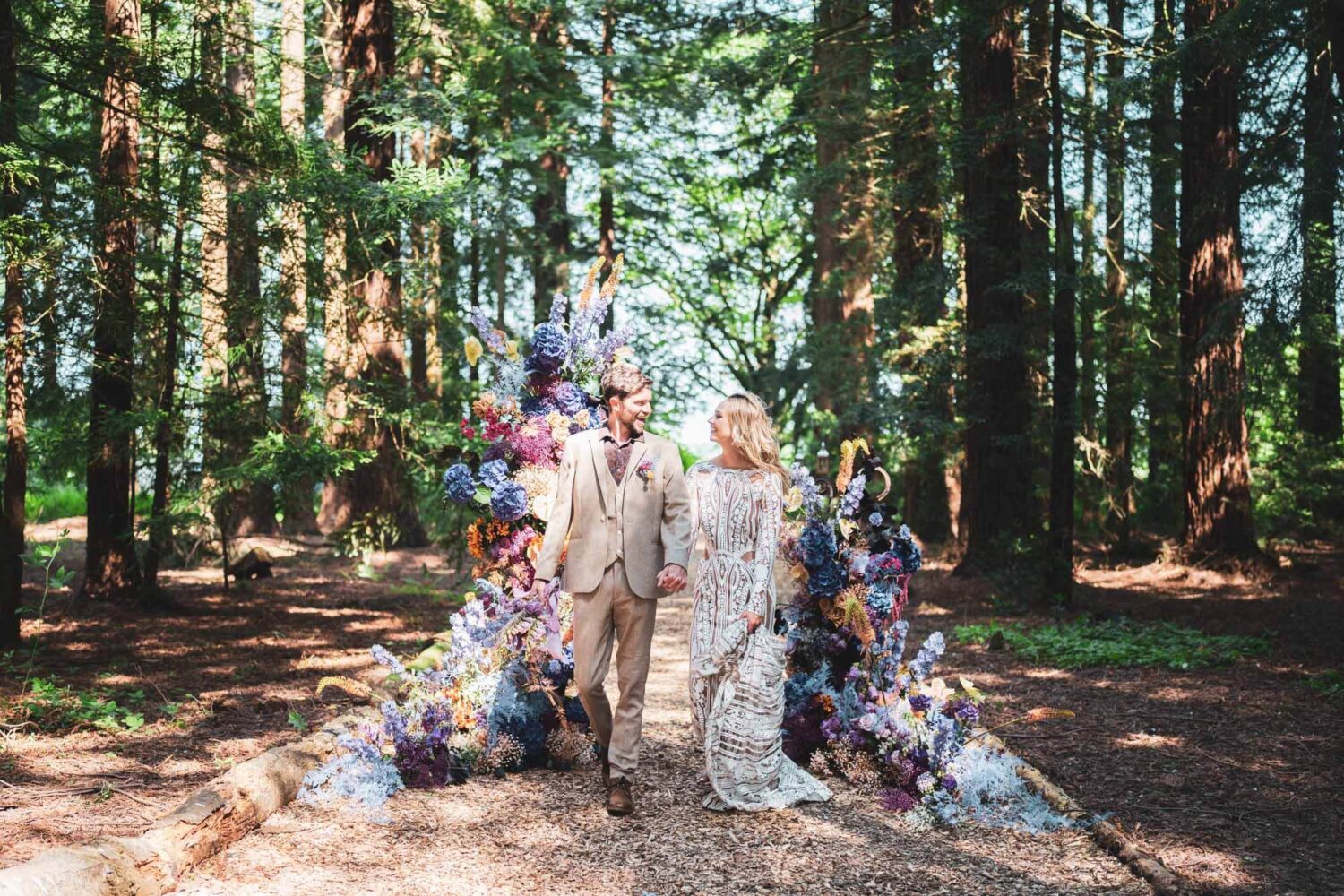 bride and groom walking through stunning redwood forest with stunning florals surrounding them looking at each other