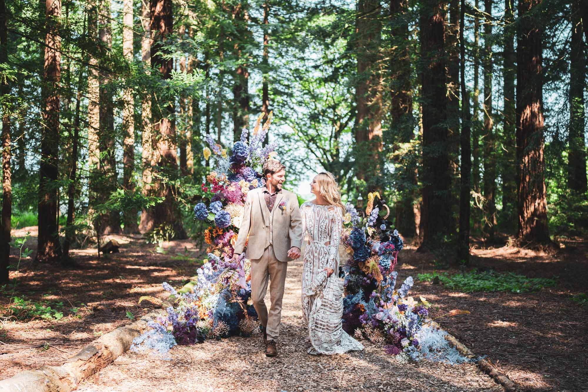 bride and groom walking through stunning redwood forest with stunning florals surrounding them looking at each other