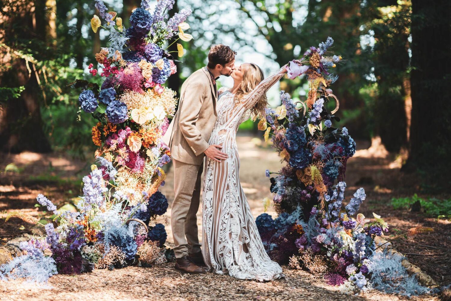 groom and bride kissing with her holding flowers up with one hand with back slightly bent backwards
