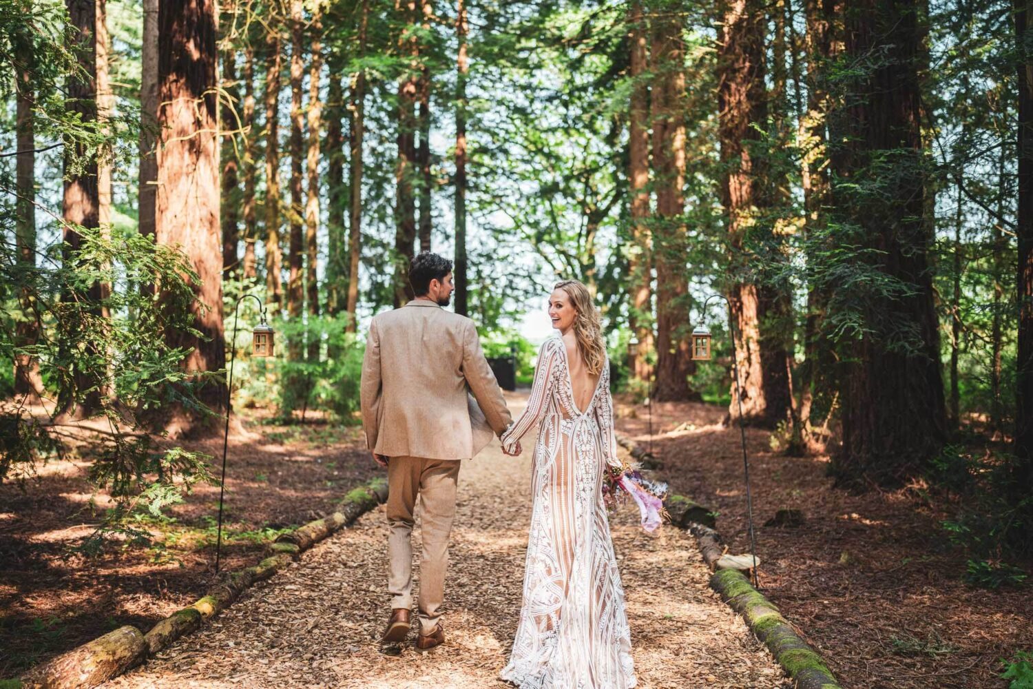 bride and groom walking away from camera with bride looking back over her shoulder in stunning redwood tree forest