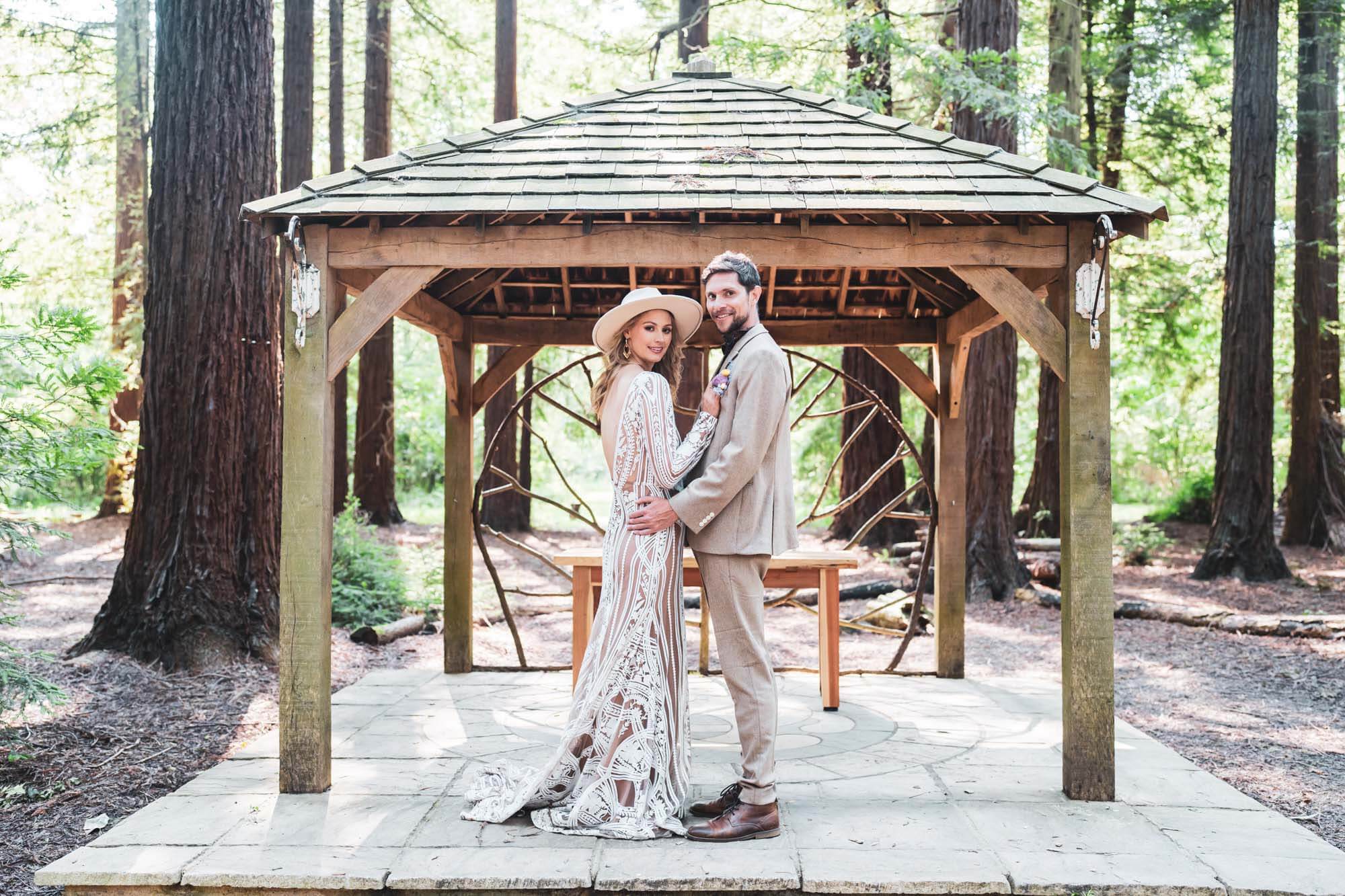 bride and groom standing in front of wooden structure looking into the camera