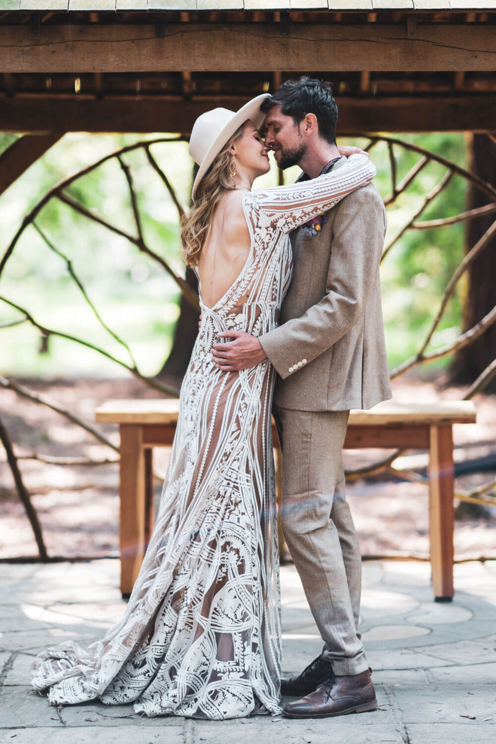 bride and groom kissing with bride's arms around groom's neck with wooden structure in background