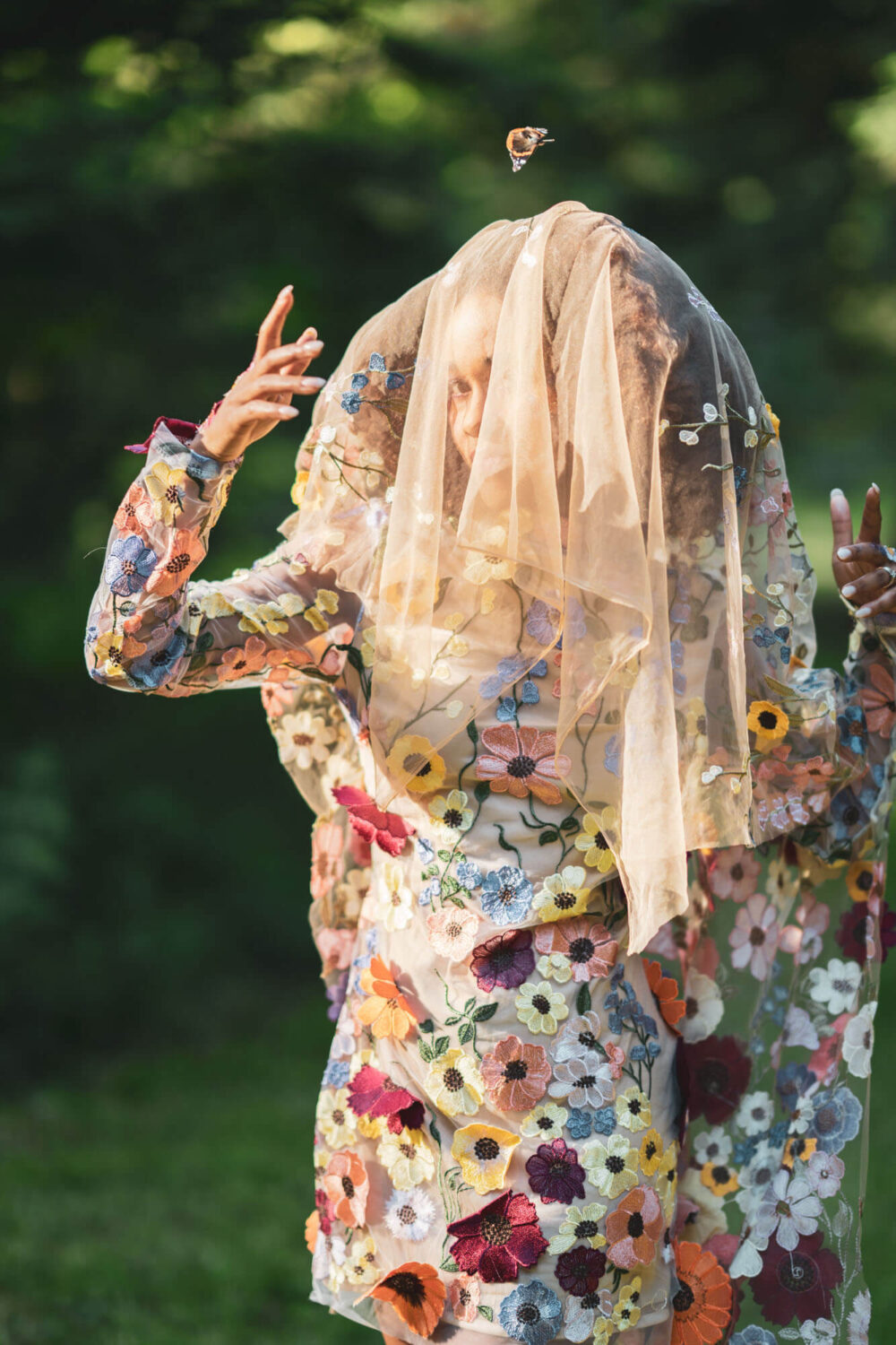 woman with floral dress and veil draped over her head sun streaming through the butterfly above her head