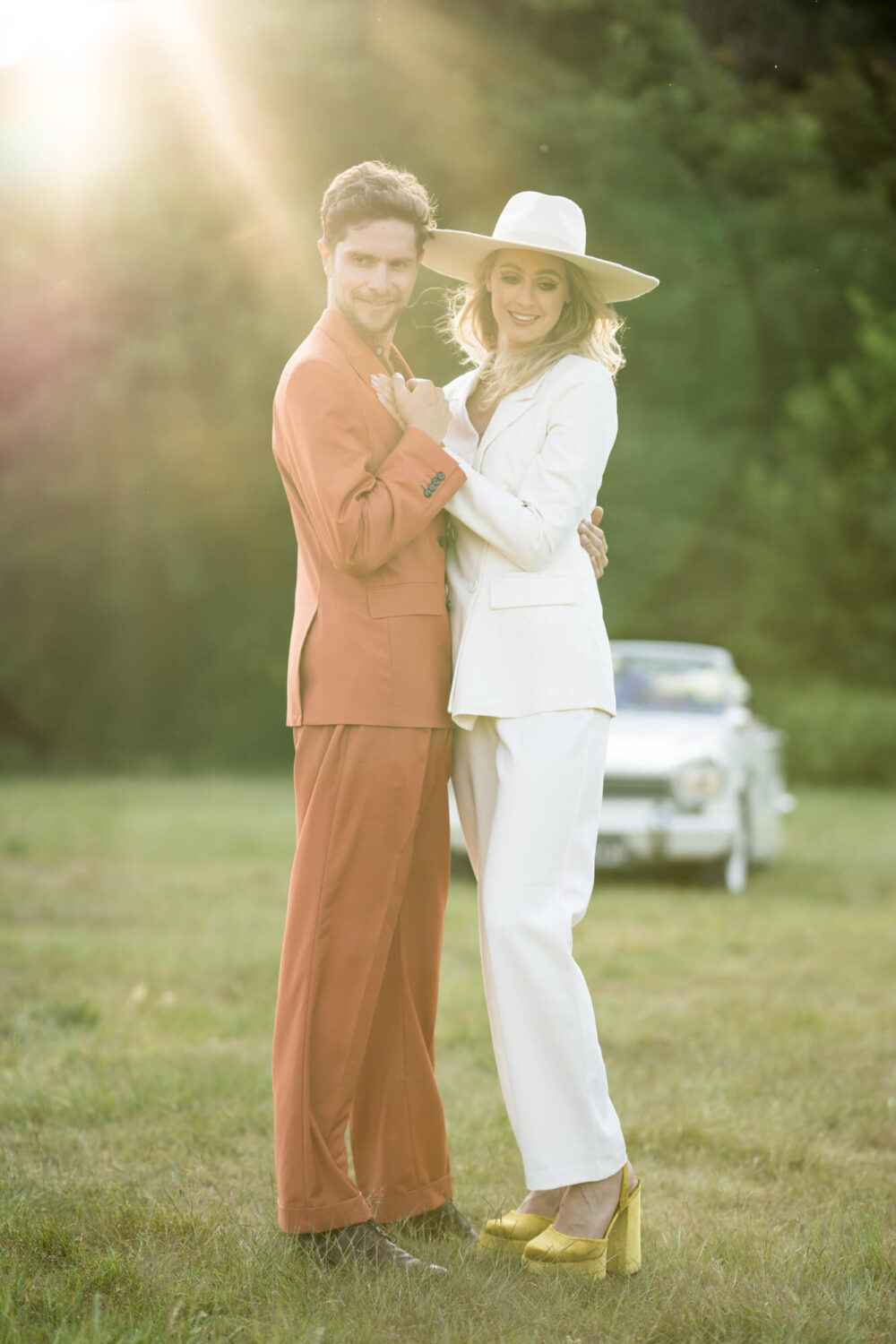 looking into the camera at golden hour the bride and groom hold hands with ray of light streaming through